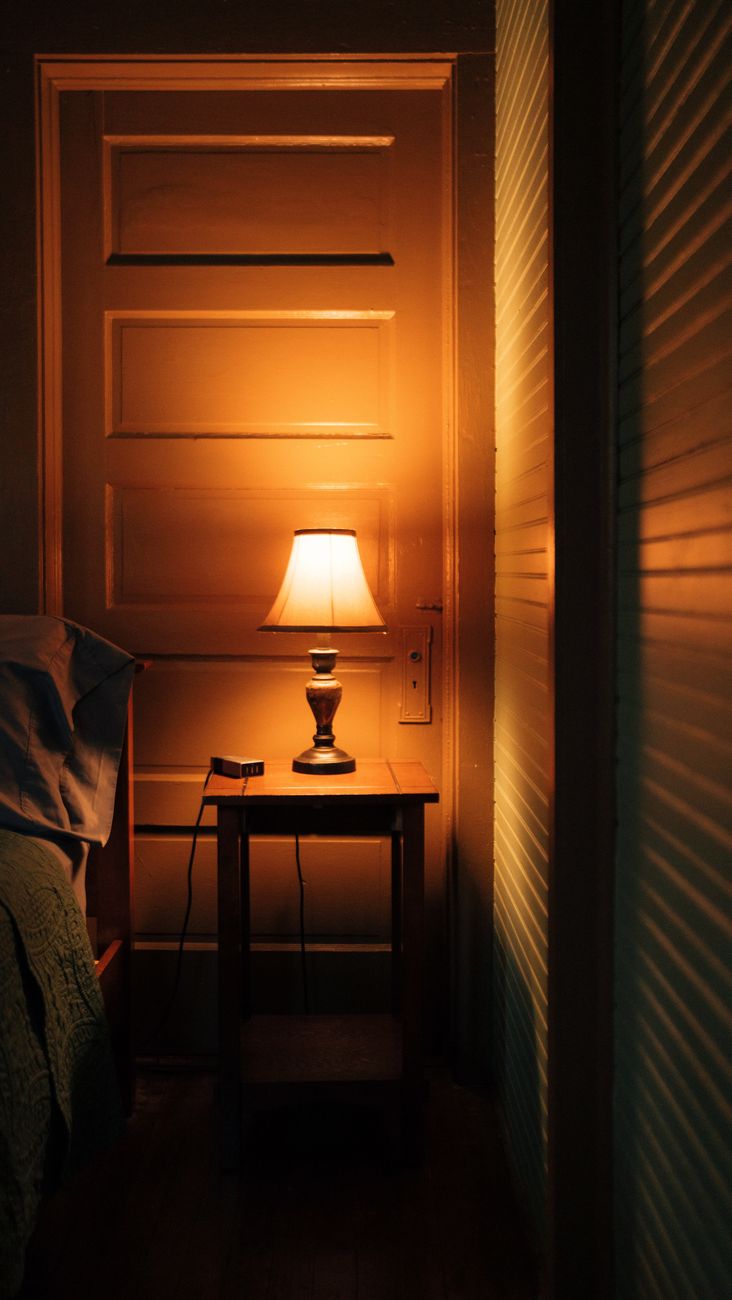 A small lamp on a nightstand glowing warmly in a cozy bedroom — the wind-down task light in place.