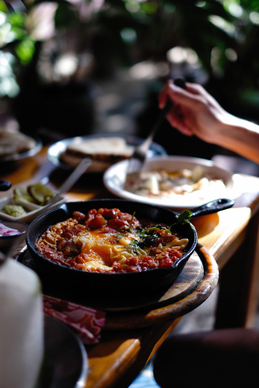 A cast iron skillet on a wooden table, holding a finished one-pan dinner — the same fixture that seared, baked, and now serves it.