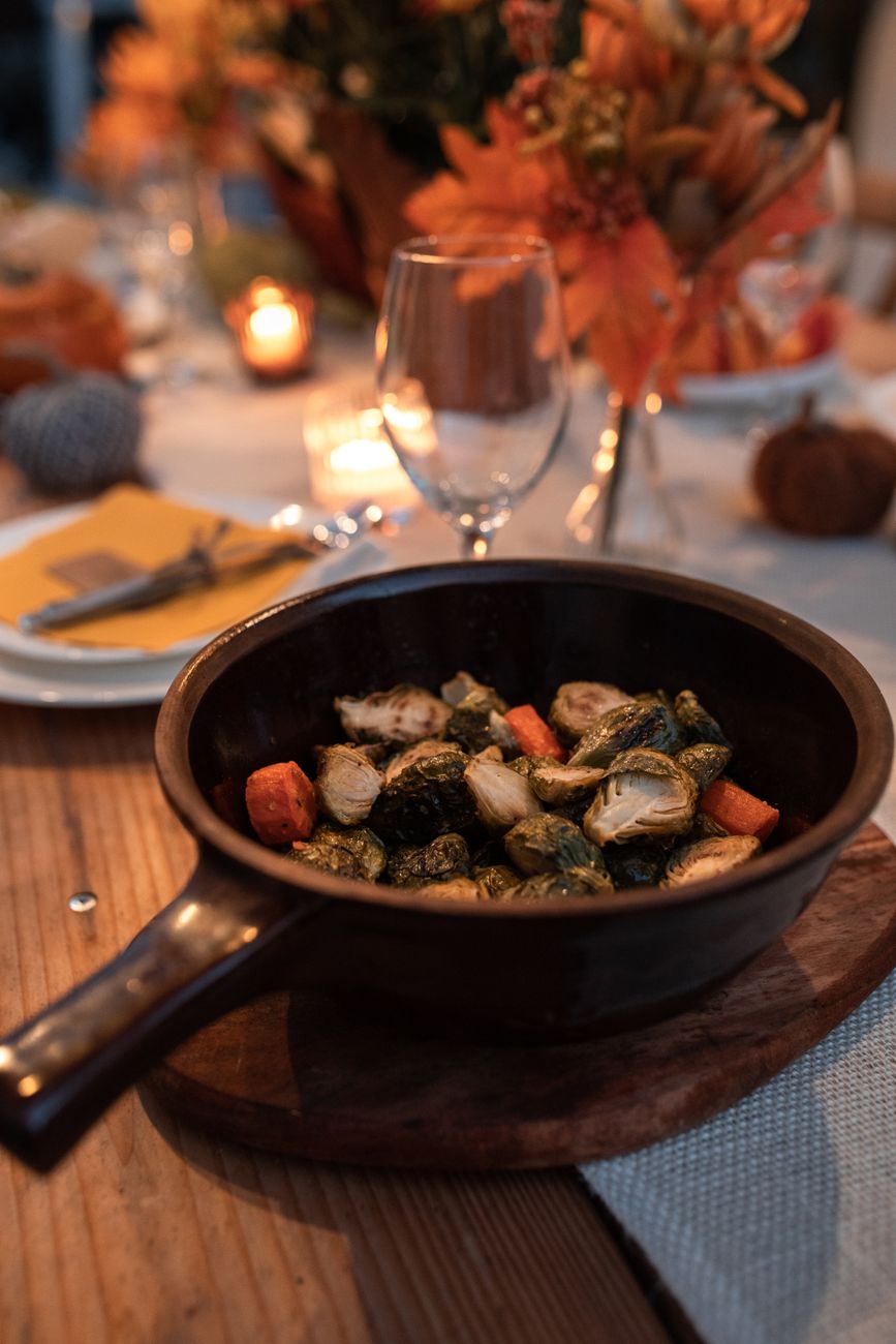 A warm autumn table set with a single pan of roasted vegetables in the center — the one-pan dinner doing dinner-party work.