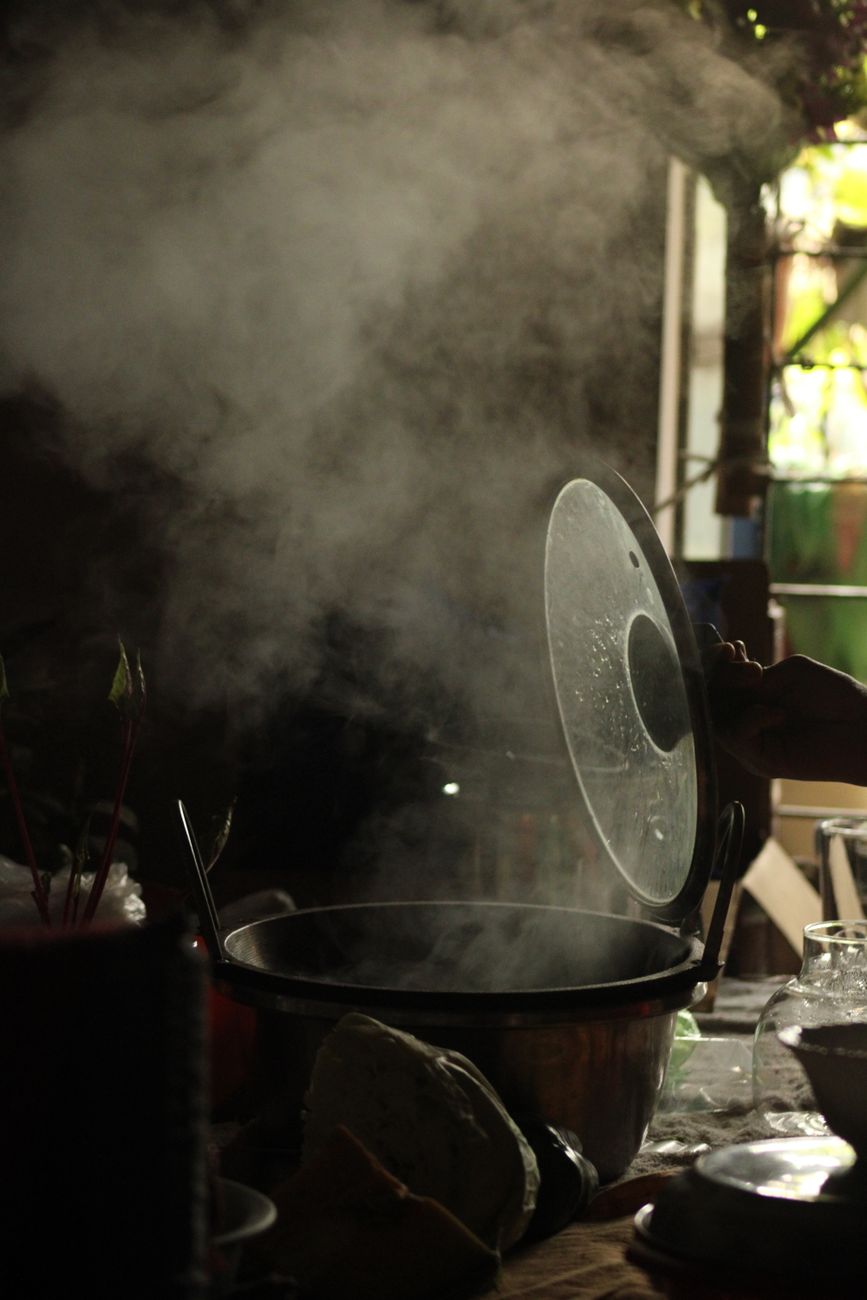 Steam rising from a single deep pot on a warmly lit stovetop — the lid-on, slow-simmer geometry that the second fixture is built around.