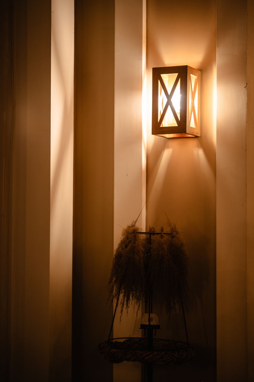 A warm wall sconce mounted above a low console with dried pampas grass, casting a soft pool against an otherwise quiet wall — the accent-layer geometry the plug-in sconce was built for.