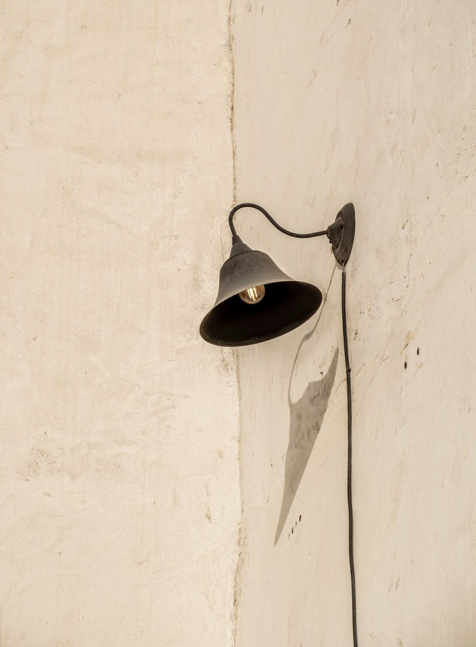 A vintage-style wall sconce on textured plaster throwing a distinct diagonal shadow — the heirloom sconce category.