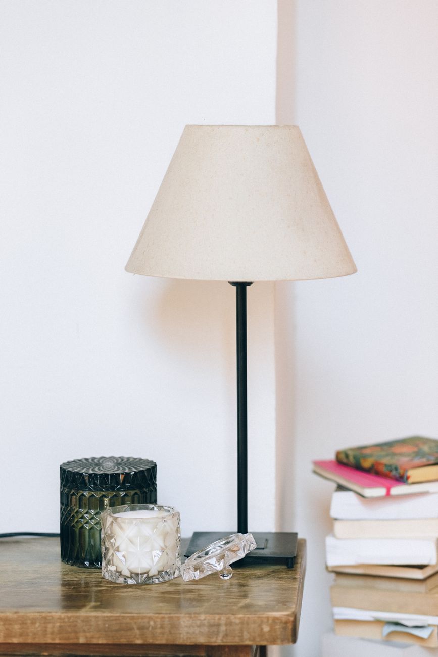 A wooden table lit by a table lamp, two unlit candles, and an open book — three independent sources at three brightness levels, the three-layer rule in a single frame.