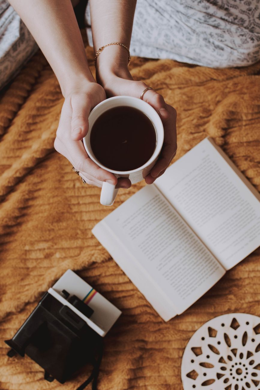 A warm morning with a coffee cup, a book, and a vintage camera — the tools of a slow morning, none of them updated for the 2026 cycle.